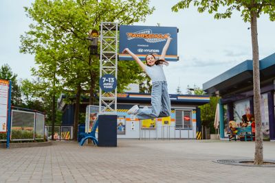 Ein Mädchen springt vor dem Eingang der Legoland Fahrschule powered by Hyundai in die Luft.