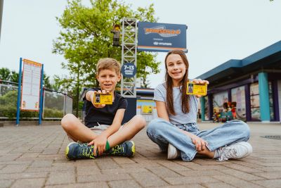 Ein Junge und ein Mädchen im Schneidersitz vor der Hyundai Fahrschule im Legoland Deutschland Resort. 