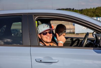 Beifahrer in einem Hyundai N-Modell mit Baseballcap mit N-Logo zeigt das Daumen-hoch-Symbol.