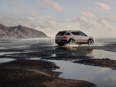 Der wasserstoffbetriebene Hyundai NEXO fährt durch seichtes Wasser am Strand.