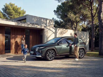 Ein Mann lehnt an dem vor einem Gebäude geparkten Hyundai TUCSON.