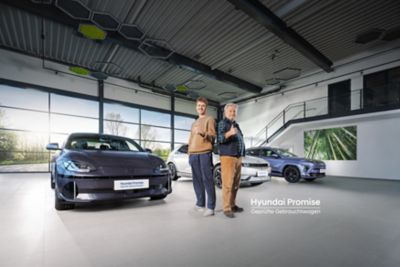 Zwei Männer stehen in einem Autohaus vor drei Hyundai Modellen und strecken den Daumen in die Höhe.
