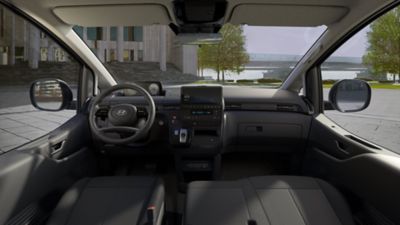 Blick in das vordere Interieur eines Hyundai STARIA, der auf einem Platz in der Nähe eines Flusses parkt. 