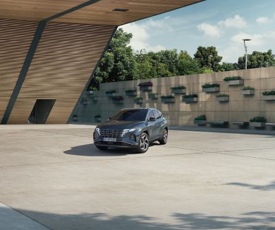 Der Hyundai TUCSON vor einem modernen Holzgebäude und einer begrünten Betonwand.