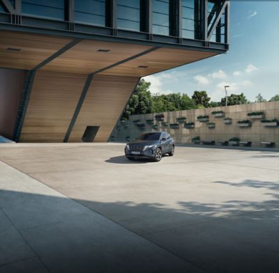Der Hyundai TUCSON vor einem modernen Holzgebäude und einer begrünten Betonwand.