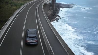 Ein Hyundai IONIQ 5, von oben gesehen, fährt über eine Brücke, die an einer Meeresküste entlangführt. 