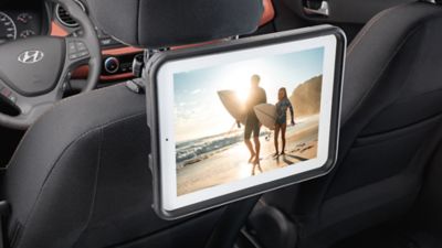 Ein Computer-Tablet, das an der Kopfstütze eines Hyundai befestigt ist, zeigt das Bild eines Mannes und eines Mädchens mit Surfbrettern. 