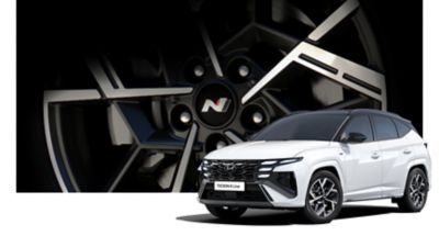 Ein weißer Hyundai TUCSON N Line vor einem vergrößerten Detail einer N Line Felge. 