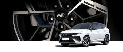 Ein weißer Hyundai TUCSON N Line vor einem vergrößerten Detail einer N Line Felge. 