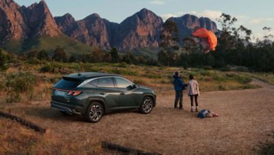 Der Hyundai TUCSON parkt vor eine Bergkulisse, daneben steht ein Paar mit Outdoorgepäck.