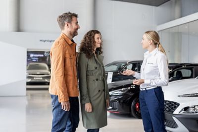 Die Mitarbeiterin eines Hyundai Autohauses berät einen Mann und eine Frau.