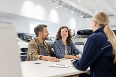 Eine Servicemitarbeiterin am Empfang eines Hyundai Autohauses berät einen Mann und eine Frau.