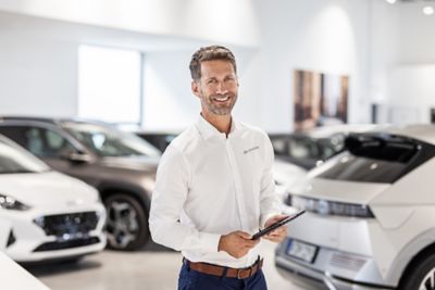 Ein Hyundai Mitarbeiter mit einem Tablet in den Händen steht im Ausstellungsraum eines Hyundai Autohauses.