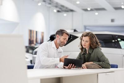 Ein Mitarbeiter eines Hyundai Autohauses berät eine Kundin am Tablet-Computer.