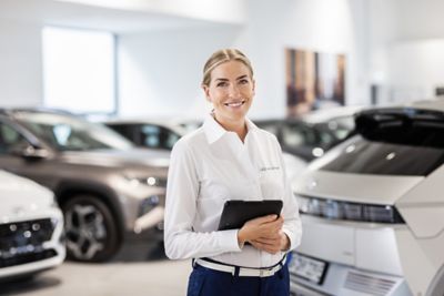 Eine Hyundai Mitarbeiterin mit einem Tablet in den Händen steht in einem Autohaus zwischen Hyundai Fahrzeugen.