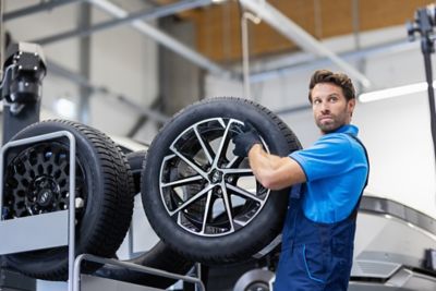 Ein Hyundai Service-Mitarbeiter holt einen Hyundai-Reifen aus der obersten Etage eines Regals.