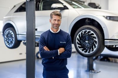 Ein Hyundai Mitarbeiter steht vor einem Hyundai Elektroauto, das sich auf einer Hebebühne befindet.