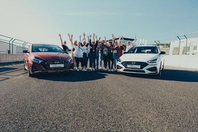 Teilnehmer der Hyundai Driving Experience stehen jubelnd zwischen zwei Hyundai i30 N.