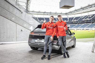 Zwei Männer stehen an der rechten Heck-Seite eines IONIQ 5, , der neben der Stadiontribüne steht.