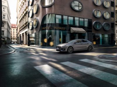 Ein grauer Hyundai i30 Fastback fährt über eine innerstädtische Kreuzung.