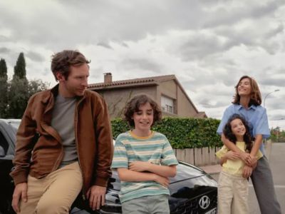 Eine Familie – Mann, Frau, Sohn und Tochter – vor ihrem Hyundai i30, der vor einem Wohnhaus parkt. 