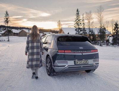 Eine Frau geht zu ihrem im Schnee geparkten IONIQ 5.