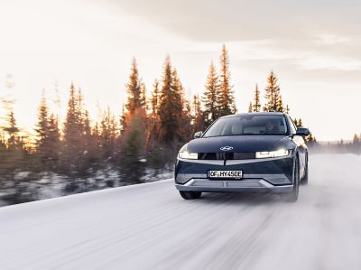 Der IONIQ 5 bei einer Fahrt über eine schneebedeckte, baumbestandene Landstraße.