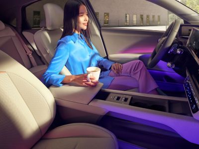Eine Frau sitzt, eine Kaffeetasse haltend, auf dem Fahrersitz eines parkenden Hyundai IONIQ 6.