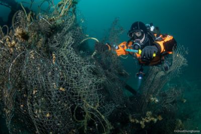 Ein Taucher schneidet ein an einem Korallenriff verfangenes, altes Fischernetz los.
