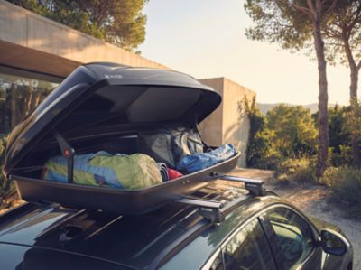 Střešní box Hyundai naplněný cestovními zavazadly upevněný na střeše vozu během letní cesty.