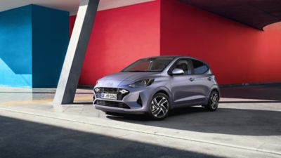 The Hyundai i10 parked in front of a red and blue wall.