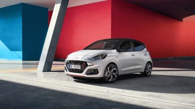 The Hyundai i10 N Line parked in front of a red wall.