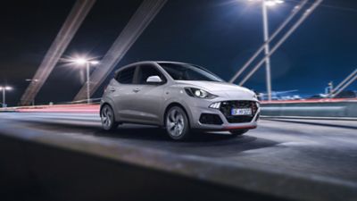 The Hyundai i10 N Line driving over a modern bridge at night.