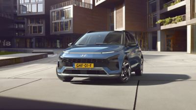 Hyundai BAYON driekwart van voren, met stadswoningen op achtergrond.