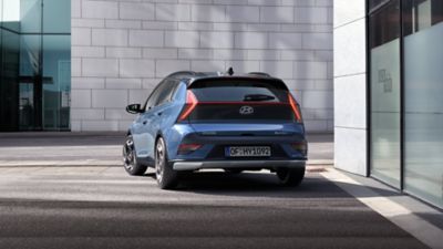Bočný pohľad na modrý Hyundai BAYON jazdiaci po ulici.