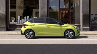 The Hyundai i20 in Lucid Lime Metallic parked in front of a shop.