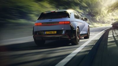 Achteraanzicht Hyundai IONIQ 5 N rijdend op asfaltweg in groene omgeving.