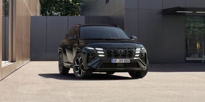 Ein Hyundai TUCSON, von vorne gesehen, parkt vor einem modernen, metallverkleideten Gebäude.