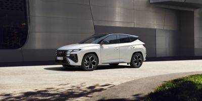 Ein weißer Hyundai TUCSON N Line, schräg von vorne gesehen, parkt vor einem metallverkleideten Gebäude.