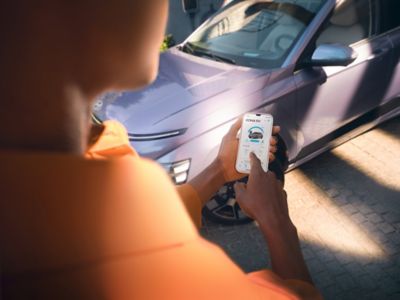 A person using a smartphone and Hyundai Bluelink app in front of a Hyundai KONA.