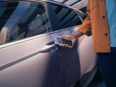 En mann holder smarttelefonen med Hyundai Digital Key 2 mot bildøren for å låse opp bilen. Foto.