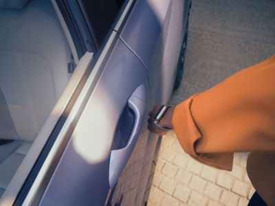 A man using a smartwatch to unlock the driver's door of the Hyundai KONA Electric.