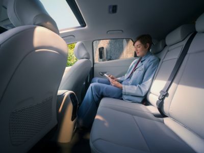 A woman using her smartphone on the back seat of the Hyundai KONA Electric SUV.