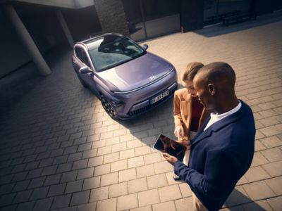 A Hyundai dealer with a tablet showing details about the Hyundai KONA Electric to a couple. 