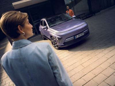 Eine Frau vor einem parkenden Hyundai KONA Elektro, in den gerade ein Mann einsteigen will.