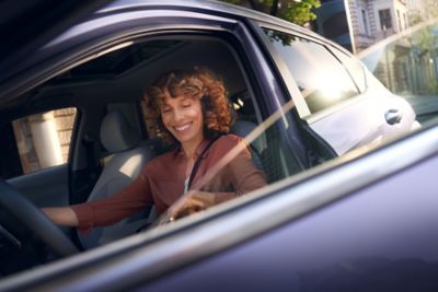 Een close-up van de Hyundai KONA Electric met een glimlachende vrouw voorin die de deur opent.