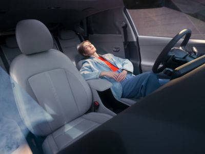 Vrouw op bestuurdersstoel van Hyundai KONA Electric SUV, rugleuning achterover.