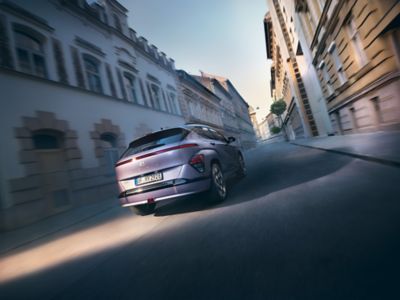 Eine Hyundai KONA Elektro, schräg von hinten aufgenommen, fährt durch eine innerstädtische Straße.