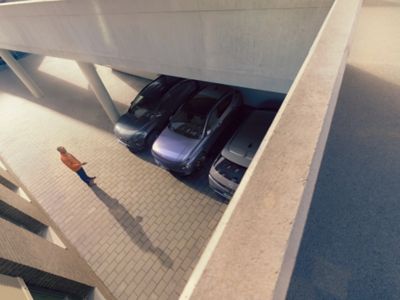 Person beobachtet, wie ein Auto sich selbst mithilfe des Remote Smart Parking Assist (RSPA) zwischen zwei andere Fahrzeuge parkiert.