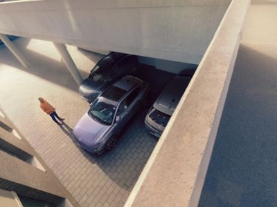 The Hyundai KONA Electric being parked backwards with a man standing next to it. 